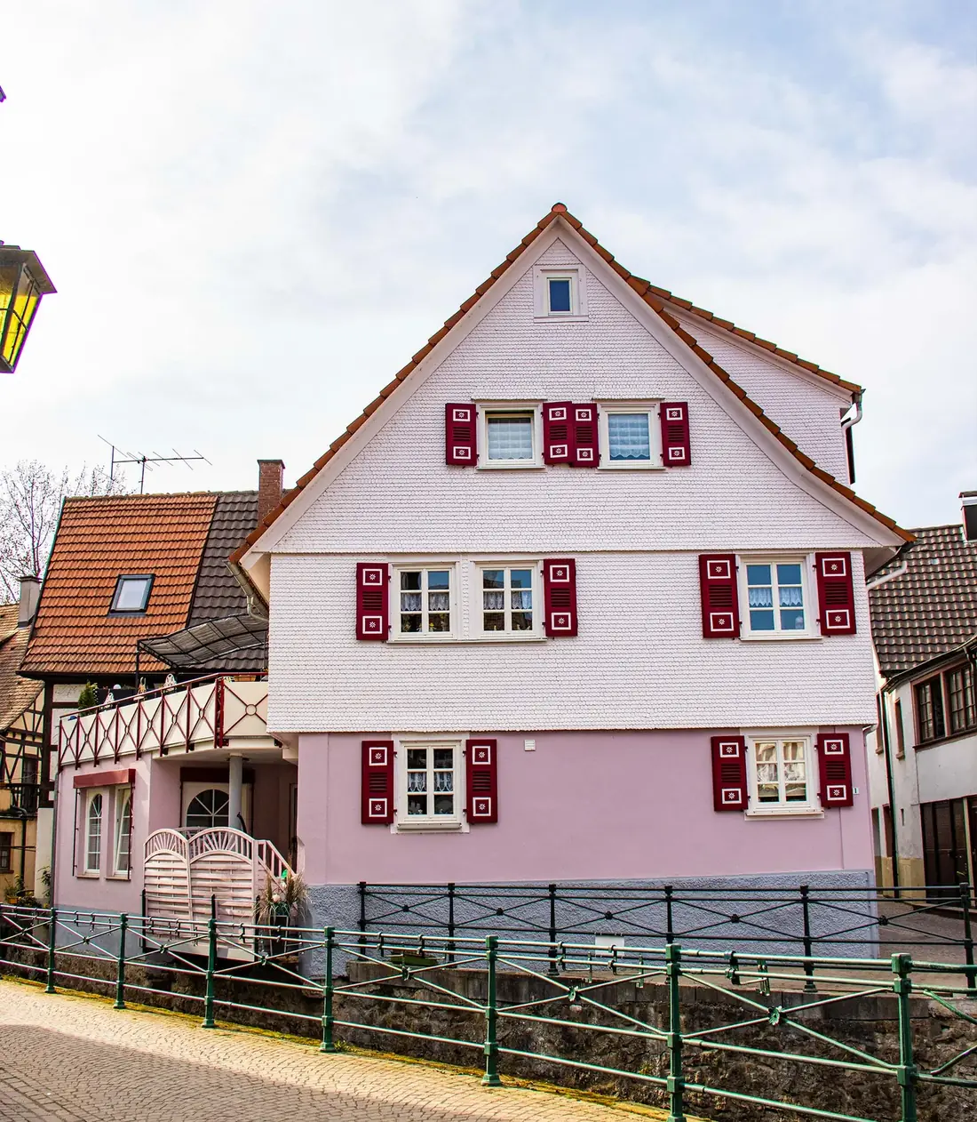 Rosa gestrichener Altbau mit roten Fensterläden an der Bachanlage